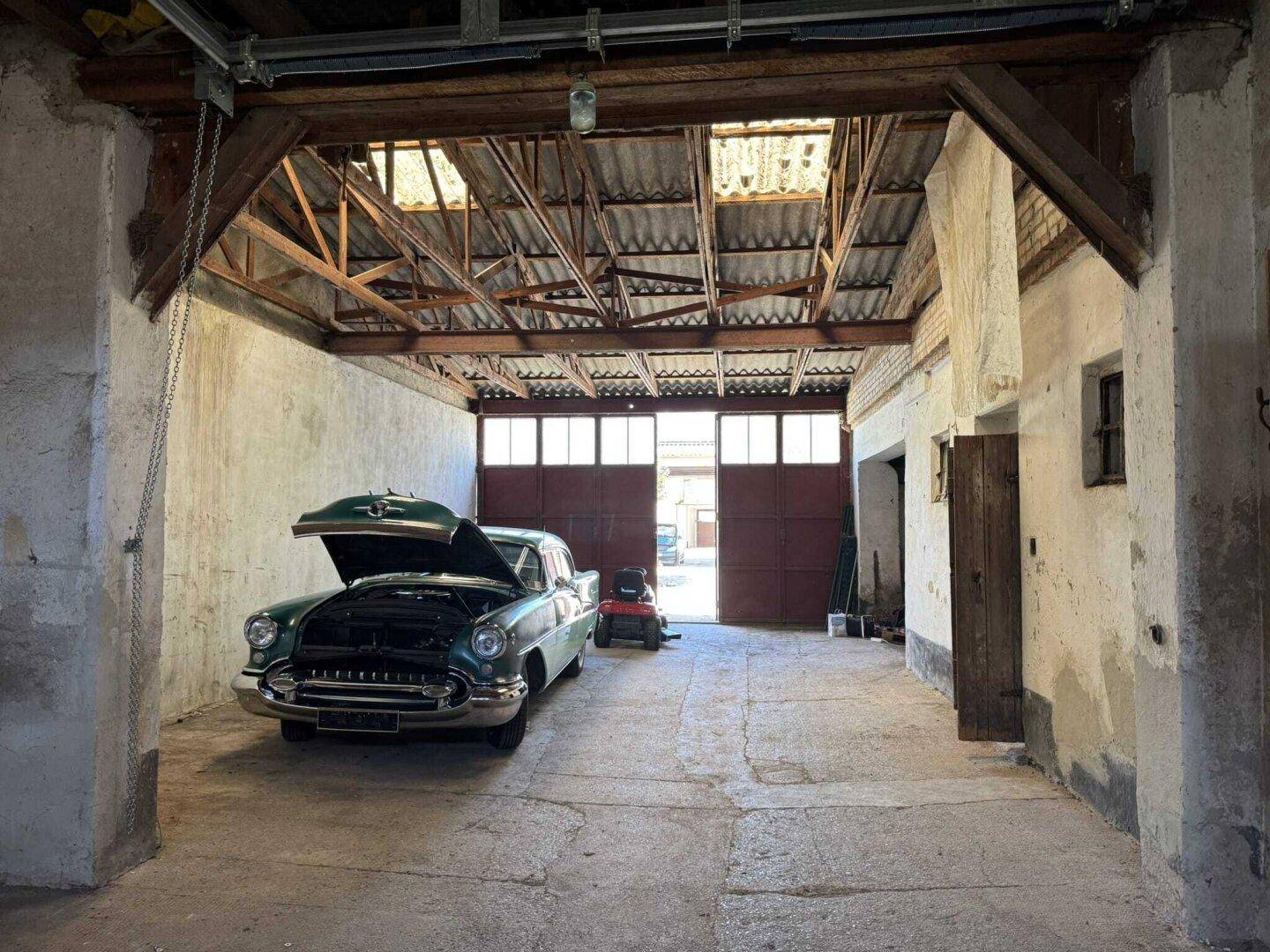 Geräumige Garage oder Werkstatt mit einem Oldtimer, Holzbalken und großen Toren.