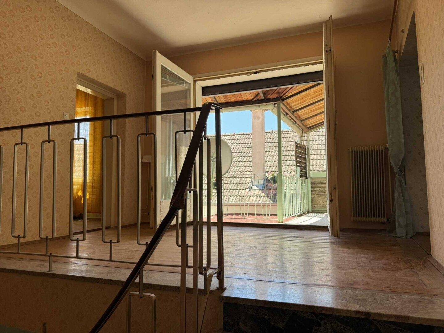 Flur mit Holzfußboden und Metallgeländer, der zu einem überdachten Balkon führt.