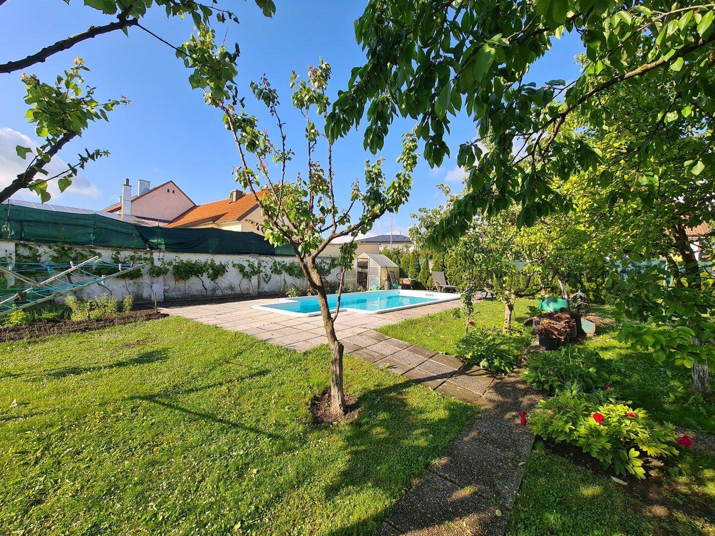 Großer Garten mit Swimmingpool, Rasenfläche und Bäumen unter blauem Himmel.