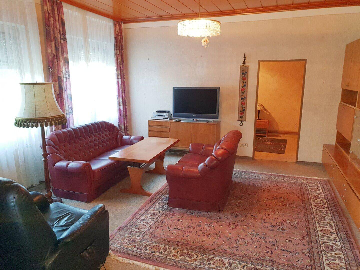 Traditionelles Wohnzimmer mit rotem Ledersofa, Teppich und Holzdecke.