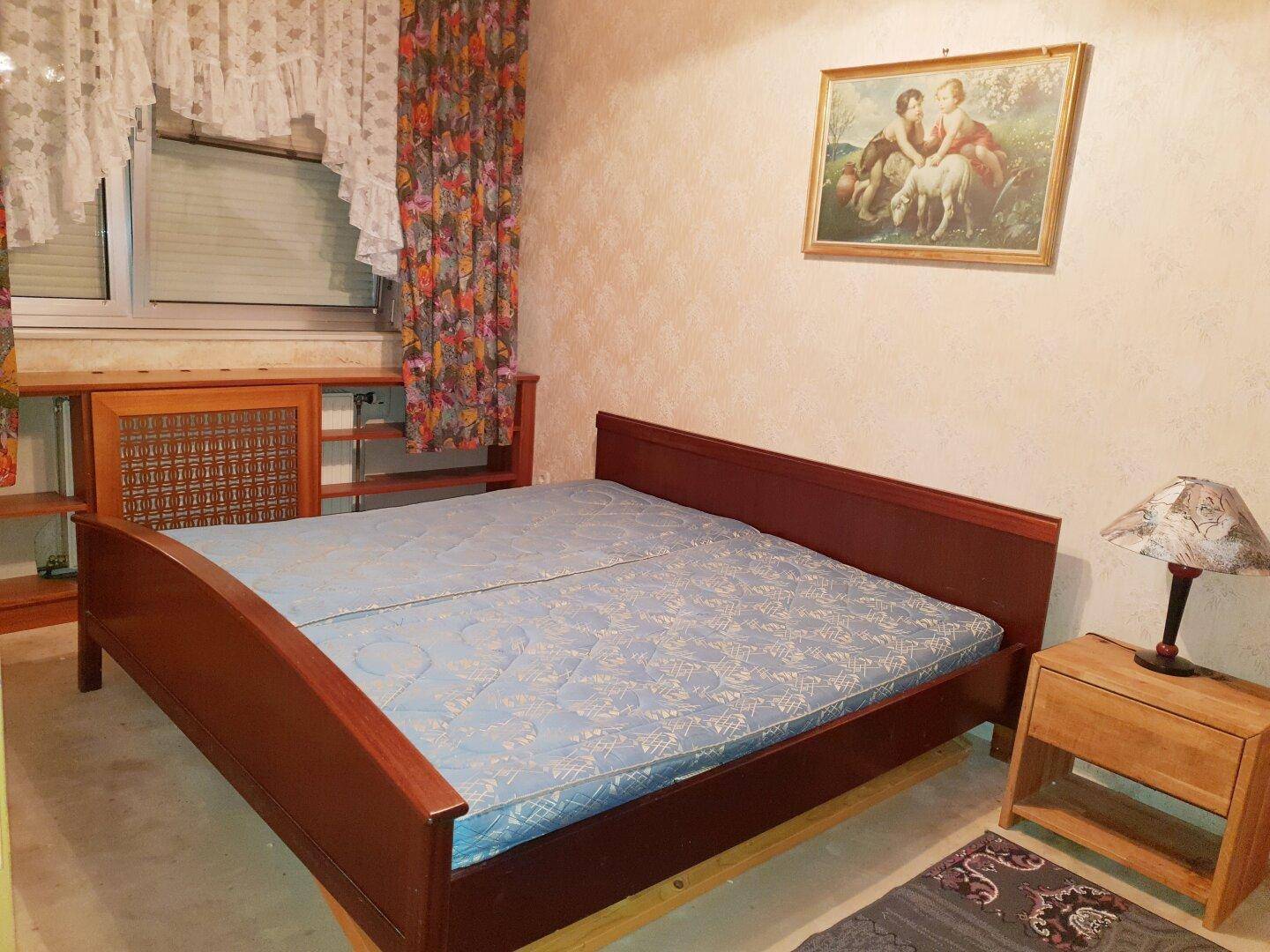 Schlafzimmer mit Holzbett, Nachttisch und Fenster, eingerichtet im traditionellen Stil.