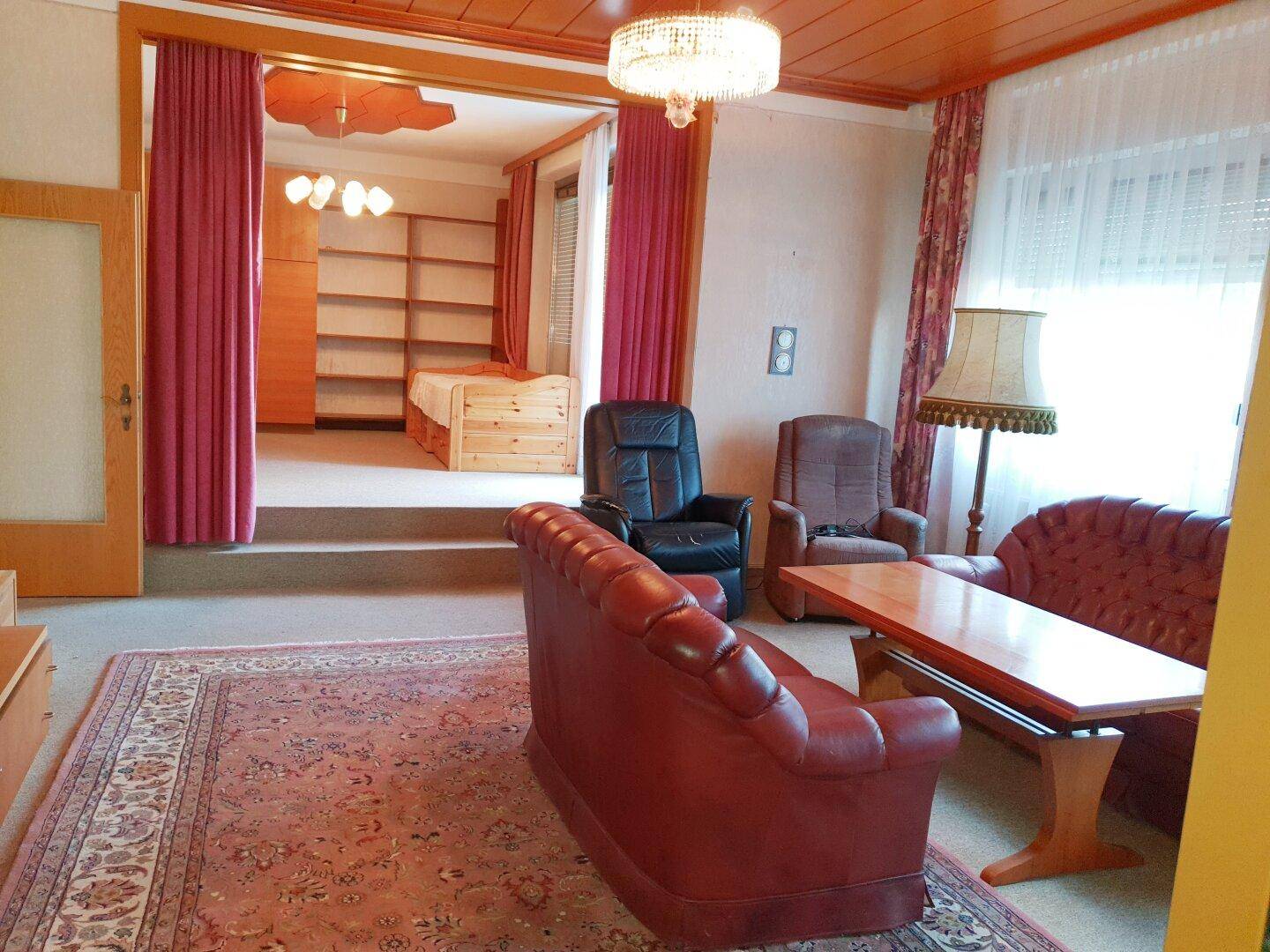 Geräumiges Wohnzimmer mit traditionellen Möbeln und angrenzendem Schlafbereich.