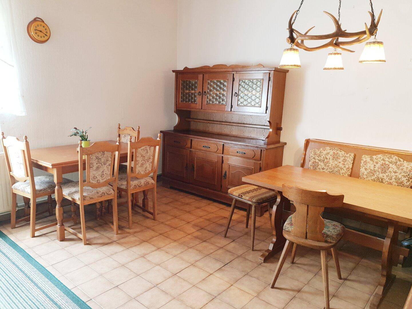Rustikaler Essbereich mit Holztisch, Stühlen, Anrichte und Geweihlampe.