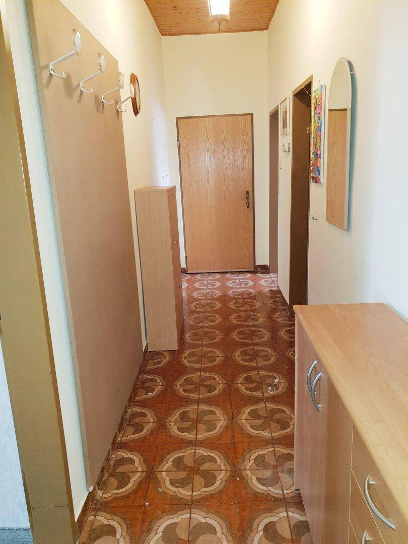 Langer Flur mit gemustertem Fliesenboden, Holzdecke und Garderobenmöbeln.