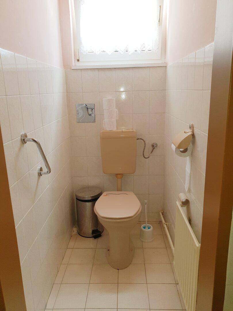Kleines WC mit Fenster, hellen Fliesen und beigefarbener Toilette.