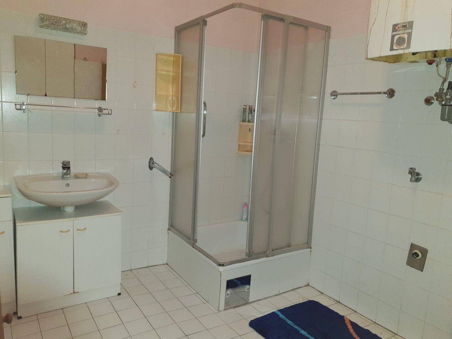 Badezimmer mit Duschkabine, Waschbecken und Boiler, gefliest in hellem Weiß.