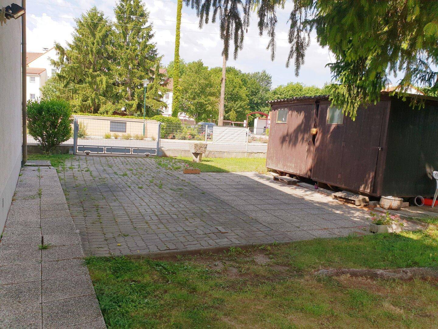 Gepflasterter Außenbereich mit einem Holzschuppen und Zugang zum Grundstück.