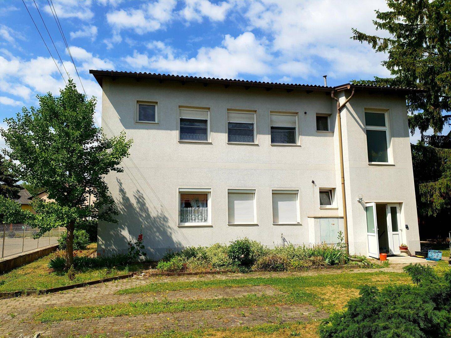 Helles Mehrfamilienhaus mit mehreren Fenstern und Rollläden, umgeben von einem kleinen Gartenbereich.