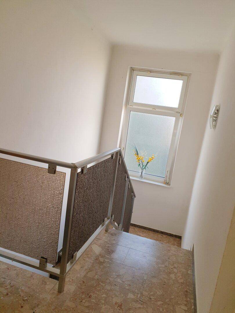 Treppenhaus mit Terrazzoboden und Fenster, das die oberen Etagen verbindet.