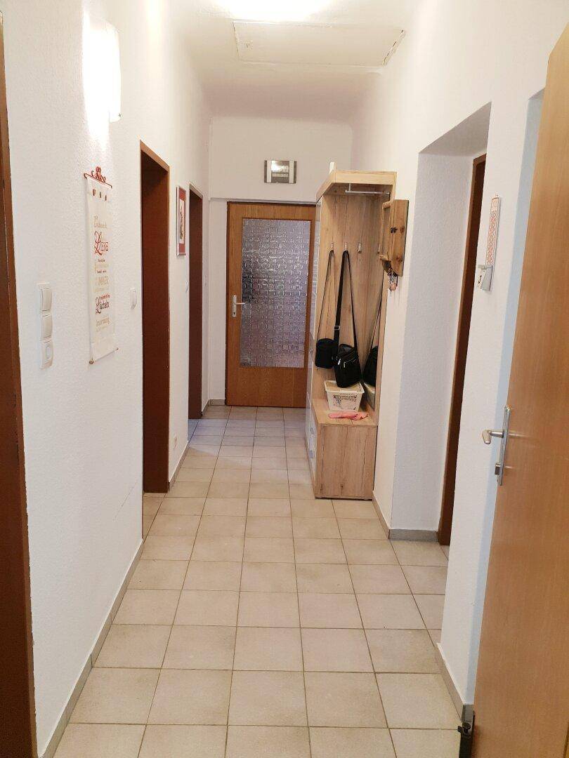 Heller Flur mit Fliesenboden und Garderobe, der zu verschiedenen Zimmern führt.