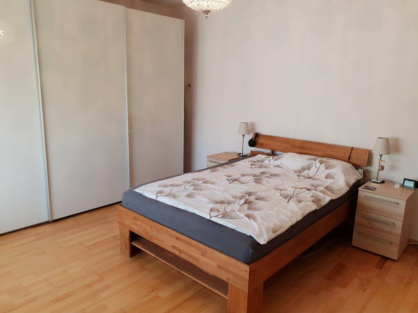 Schlafzimmer mit hellem Holzbett, Nachttischen und großem weißen Kleiderschrank.
