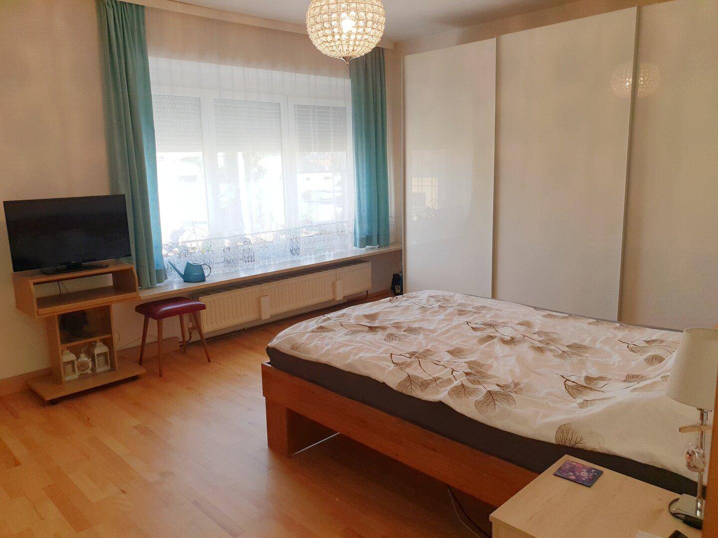 Schlafzimmer mit Holzbett, weißem Schiebetürenschrank und großem Fenster.