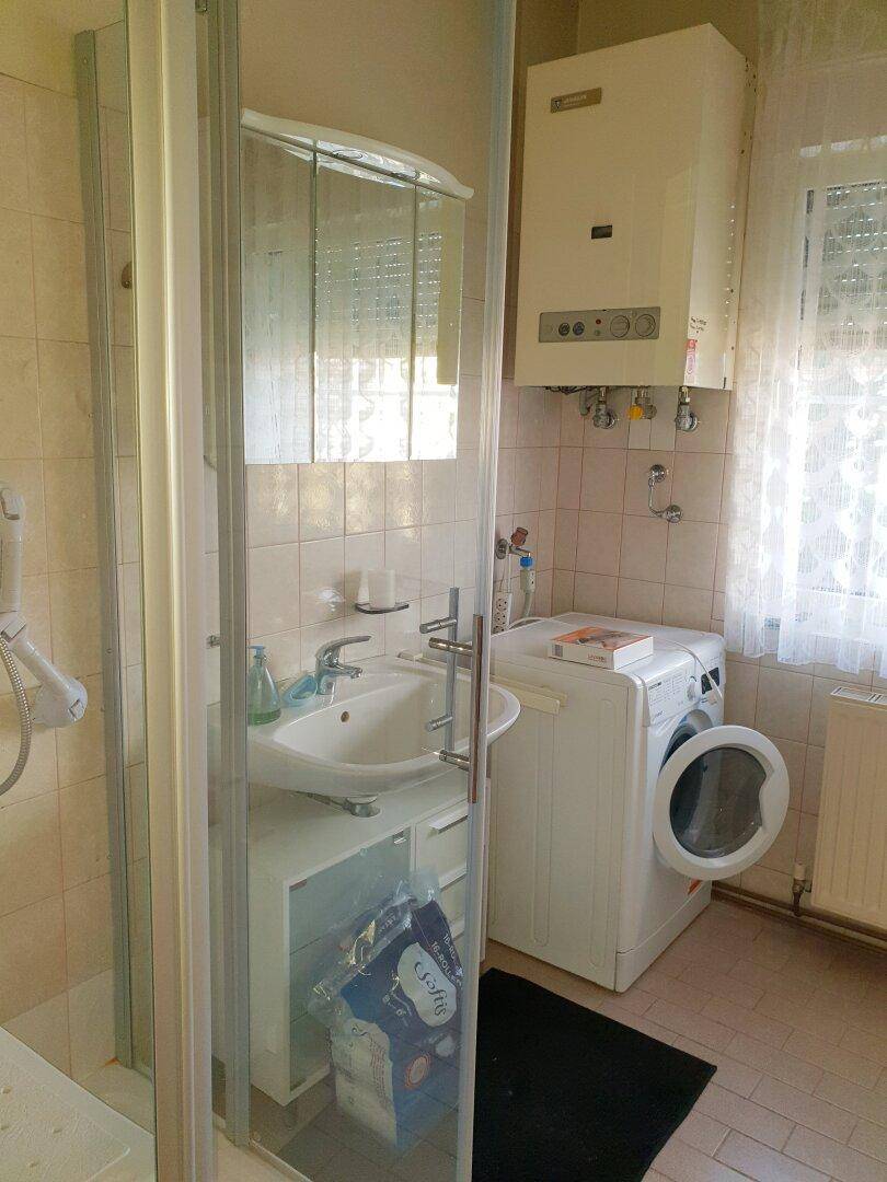 Badezimmer mit Duschkabine, Waschbecken, Waschmaschine und Gastherme.
