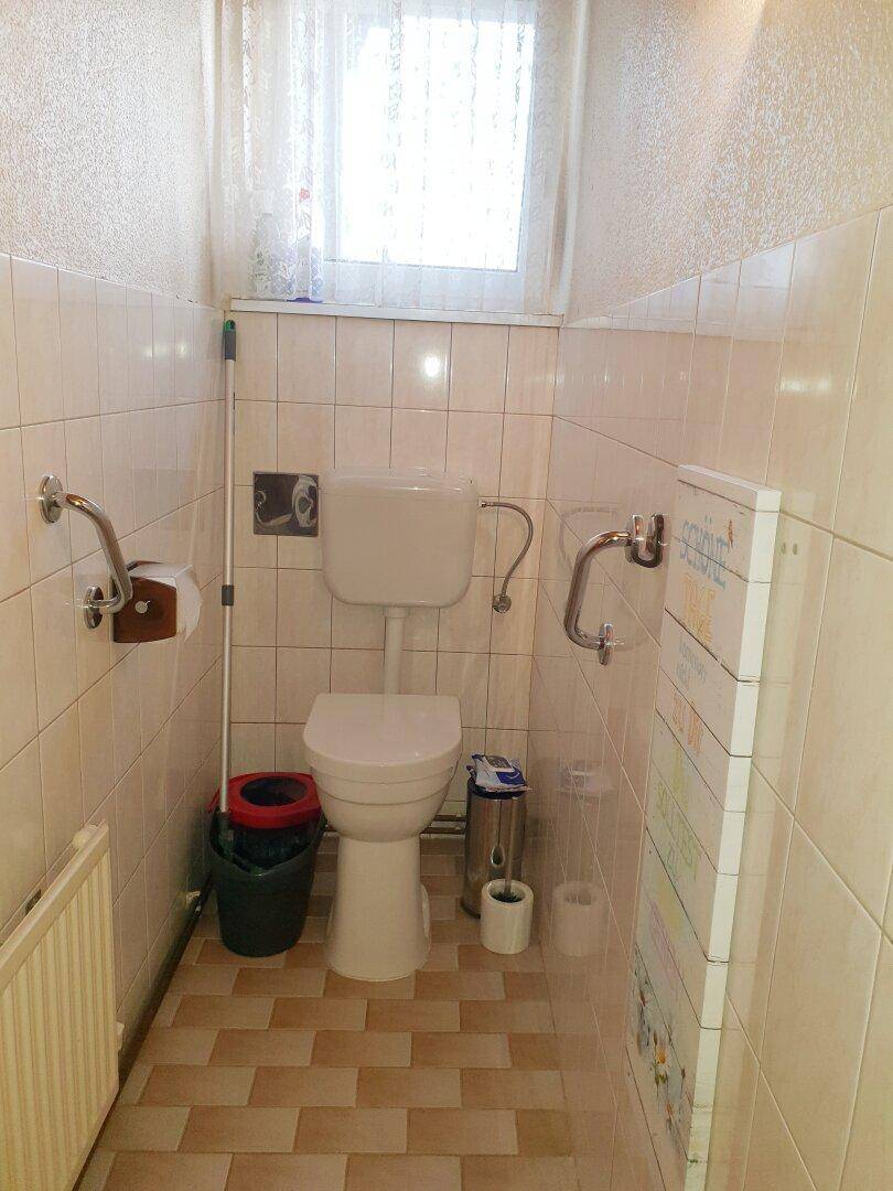 Separate Toilette mit Fenster, hellen Fliesen und Haltegriffen für Komfort.