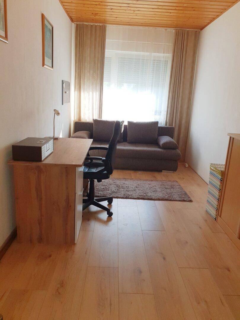 Helles Zimmer mit Schreibtisch, Sofa und Holzdecke, nutzbar als Büro oder Gästezimmer.