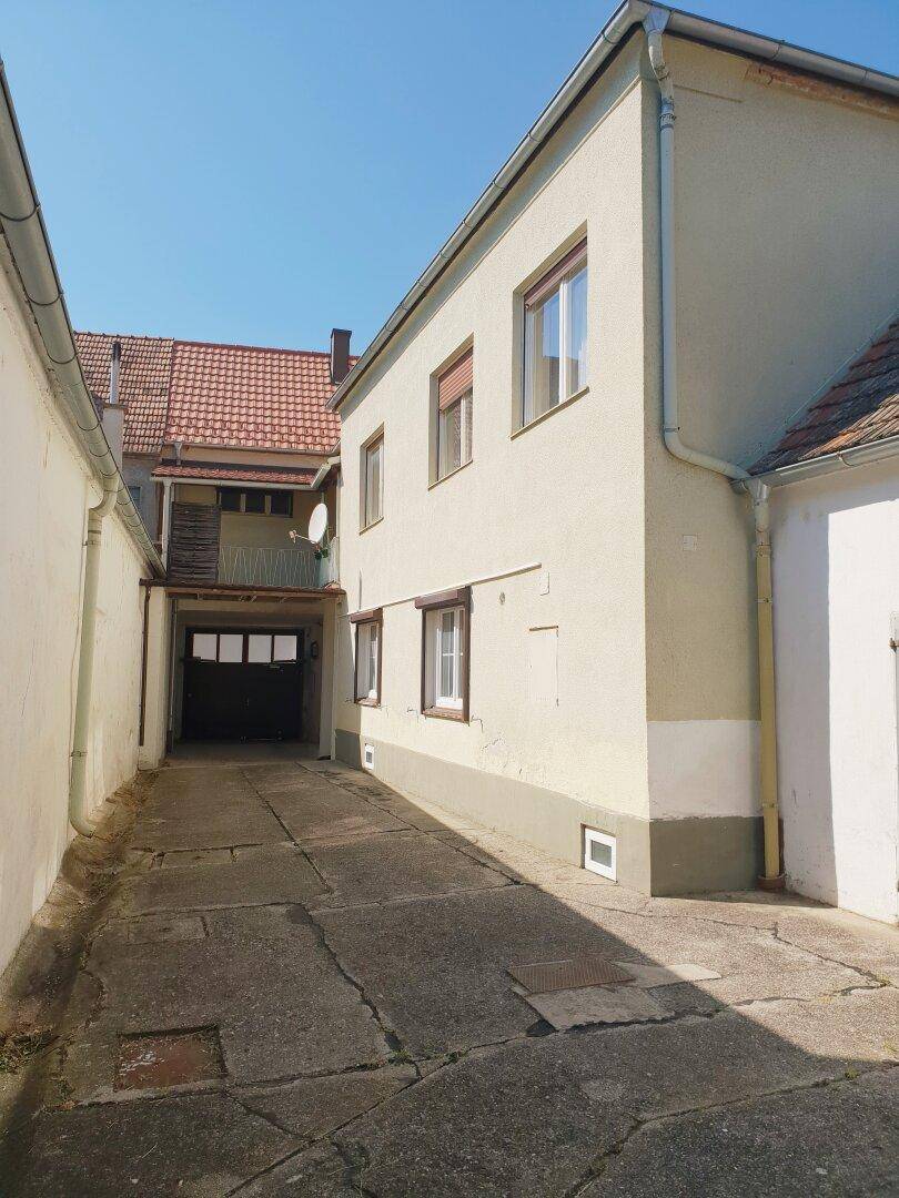 Schmaler Betonweg zwischen zwei Gebäuden, der zu einem überdachten Bereich führt.