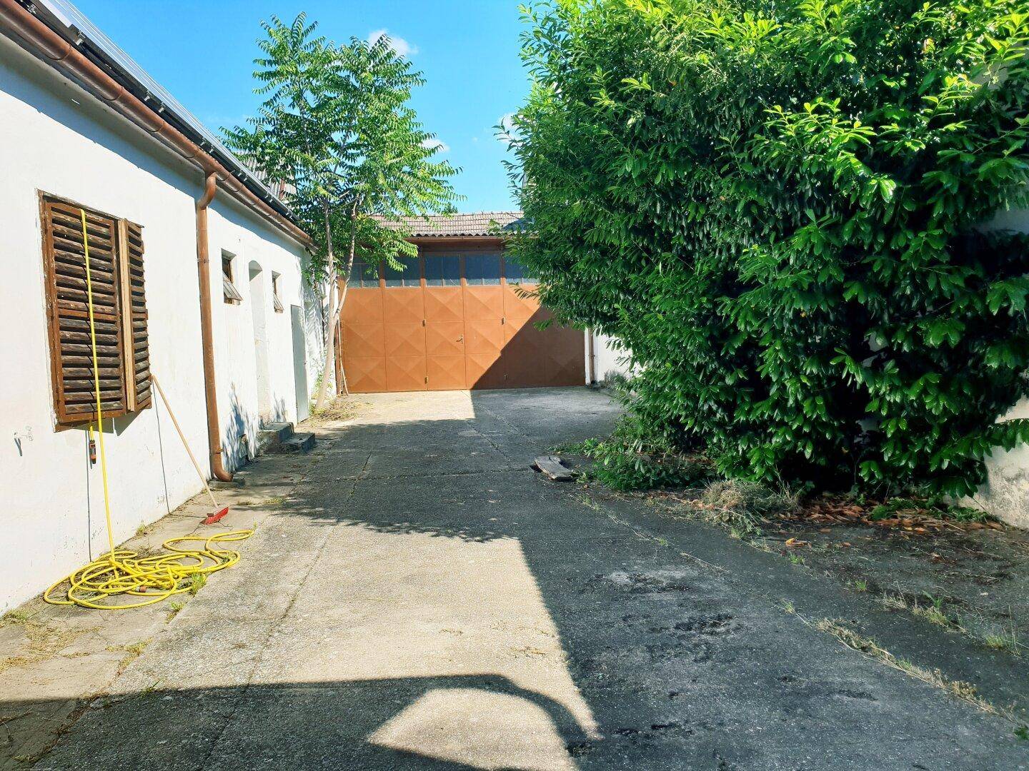 Betonierte Zufahrt zu einer Garage, umgeben von einem weißen Gebäude und üppigem Grün.