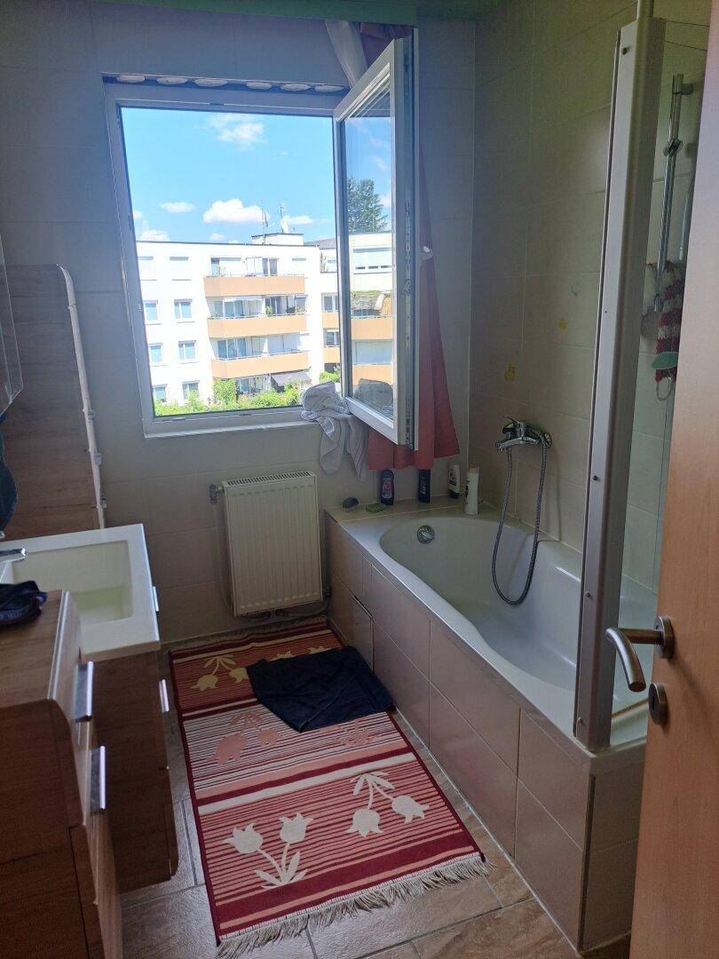 Badezimmer mit Badewanne, Duschabtrennung und einem Fenster mit Blick auf Gebäude.