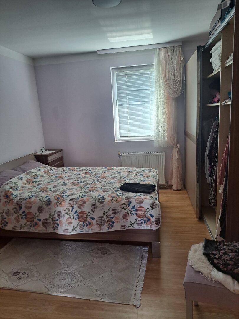 Schlafzimmer mit Doppelbett, offenem Kleiderschrank und Fenster mit Jalousien.
