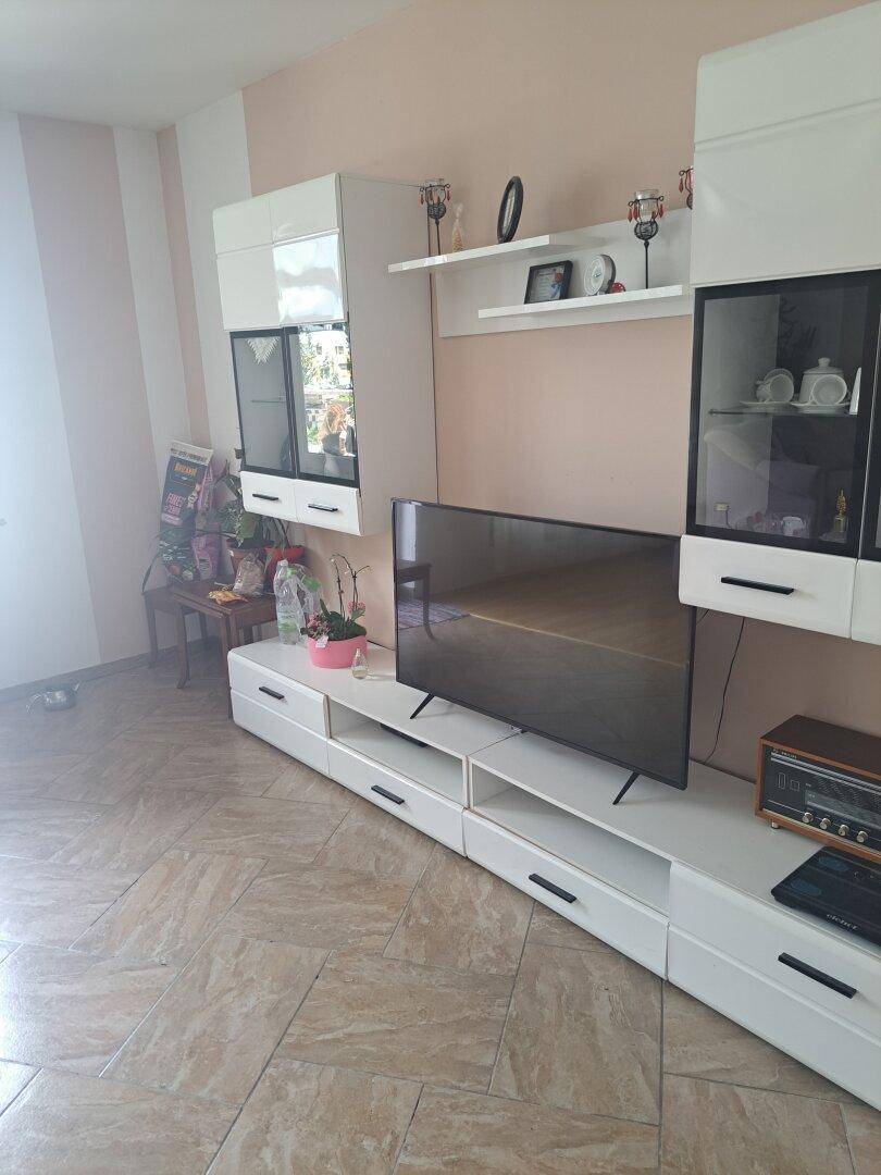 Wohnzimmer mit modernem, weißem TV-Möbel und Fliesenboden in hellem Beige.