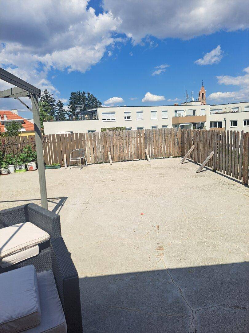 Große, gepflasterte Terrasse mit Sitzgelegenheiten und einem Holzzaun im Hintergrund.
