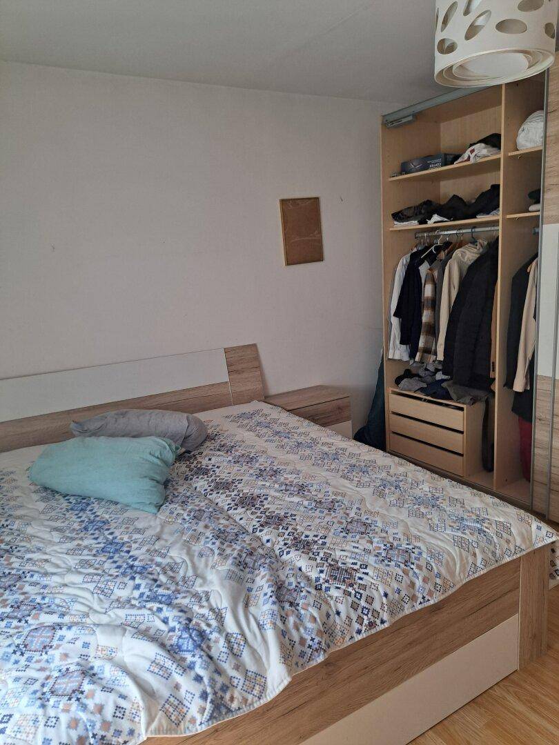 Schlafzimmer mit Bett und einem offenen Kleiderschrank aus hellem Holz.