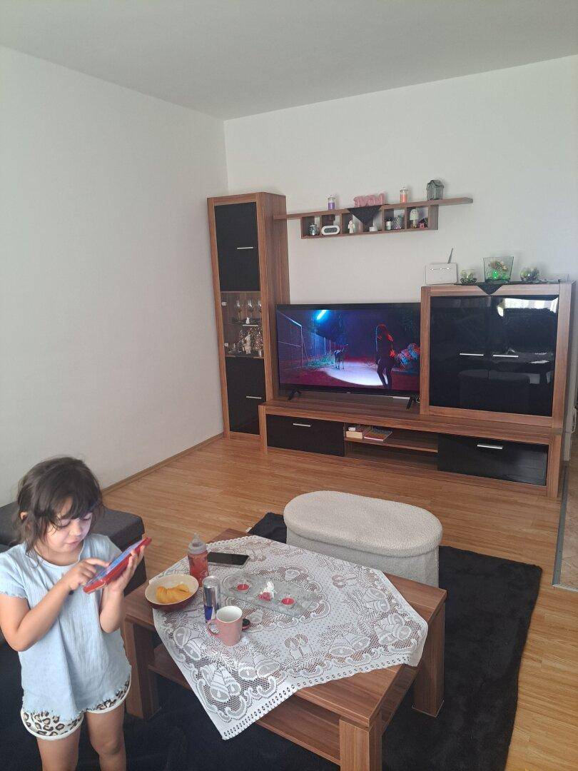 Wohnzimmer mit TV-Möbel, Holztisch und einem kleinen Mädchen im Vordergrund.