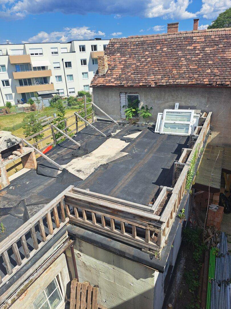 Dachterrasse in Renovierung mit Blick auf umliegende Gebäude und den Himmel.