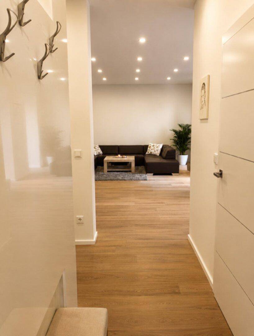 Heller Flur mit Holzboden und Garderobe, der in einen offenen Wohnbereich führt.