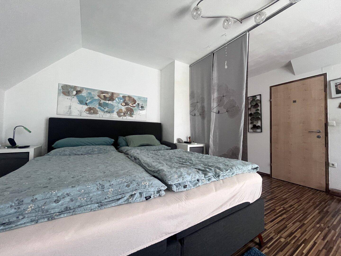 Schlafzimmer mit Doppelbett und Nachttischen, abgetrennt durch einen dekorativen Vorhang.