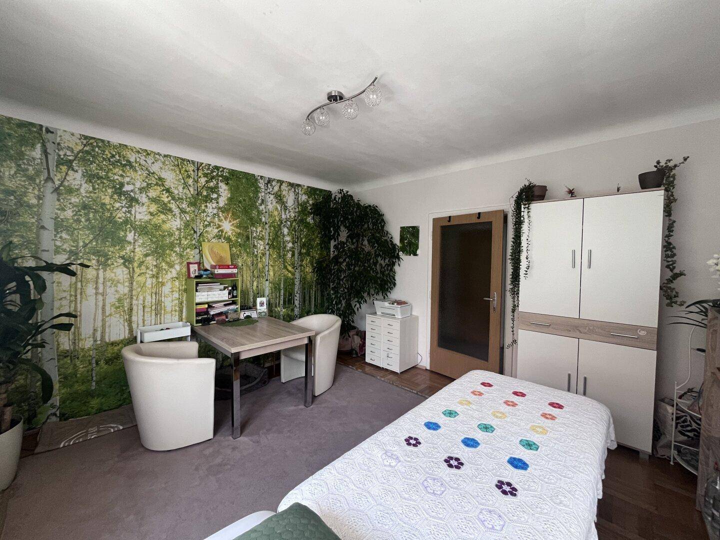 Vielseitiger Raum mit Waldtapete, Schreibtischbereich und einer Liege, ideal für Büro oder Praxis.