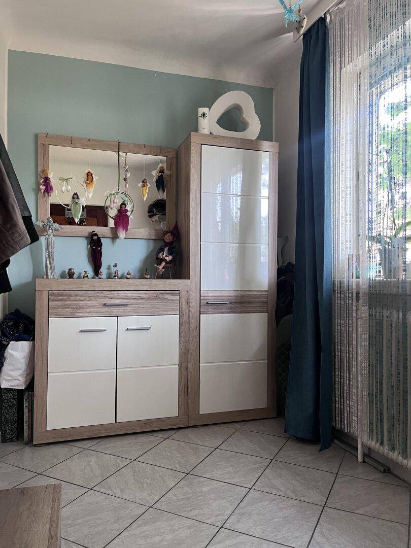 Eingangsbereich mit Fliesenboden, Garderobe und einem Spiegel, hell durch das Fenster.