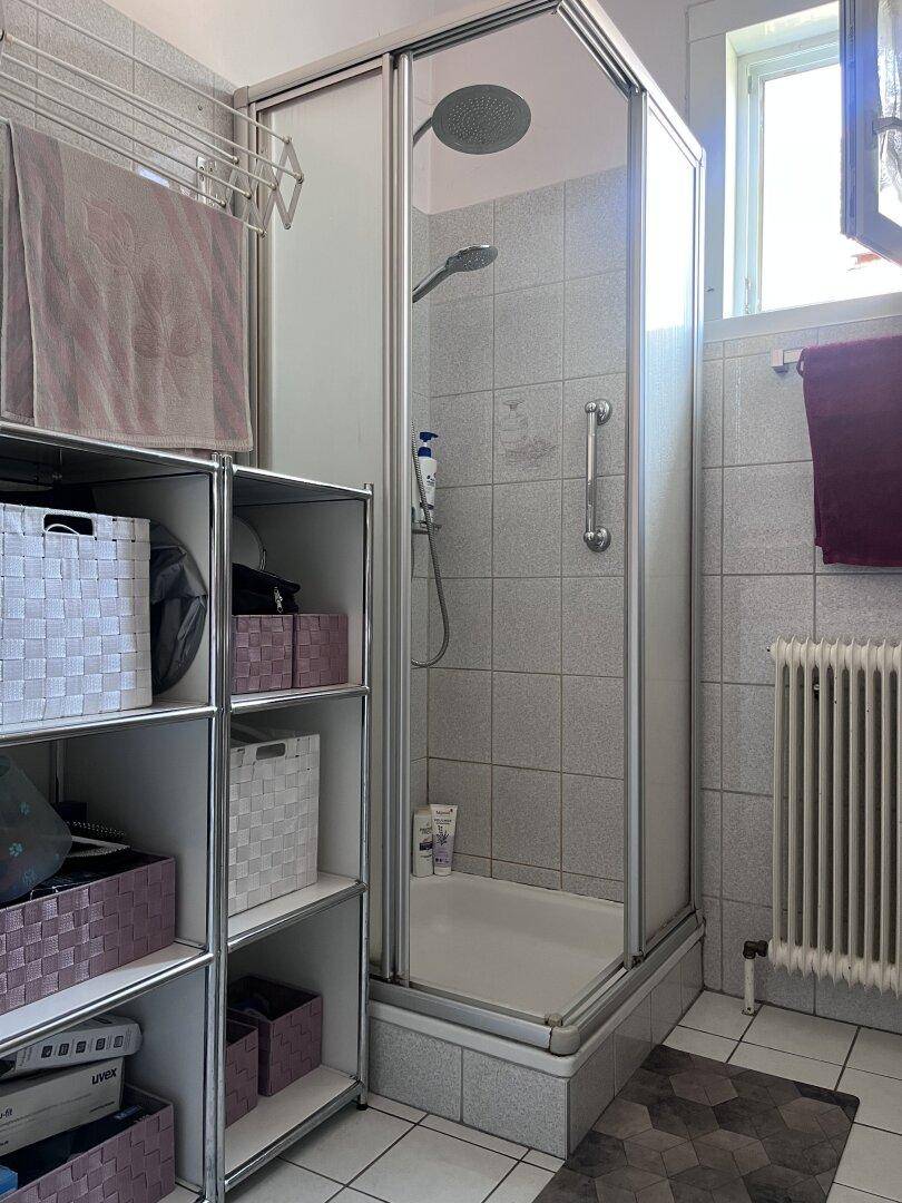 Duschbereich im Badezimmer mit Glasabtrennung, Duschkopf und Haltegriff, funktional gestaltet.