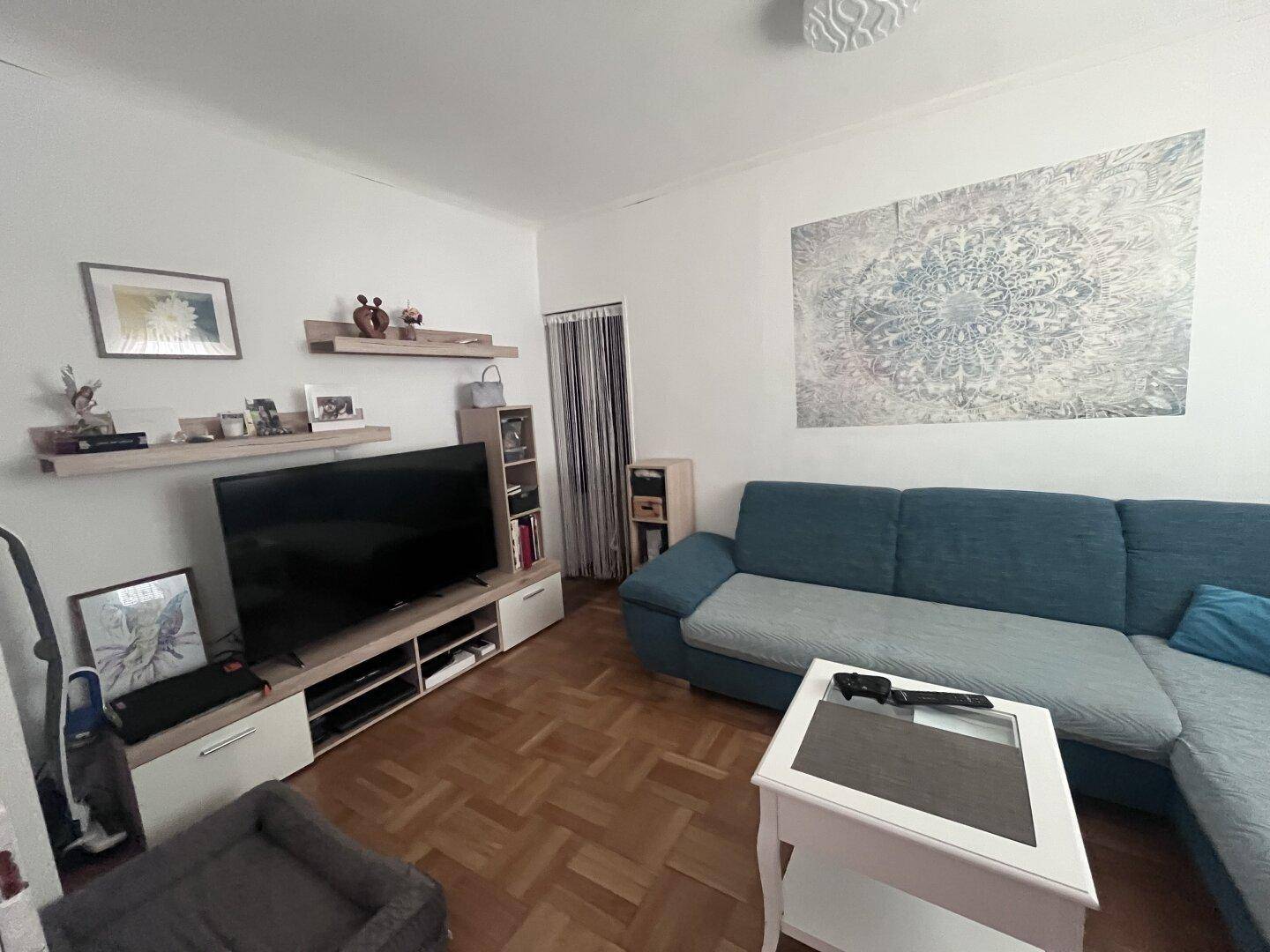 Gemütliches Wohnzimmer mit Sofa, Fernseher und Parkettboden, dekoriert mit Wandregalen.