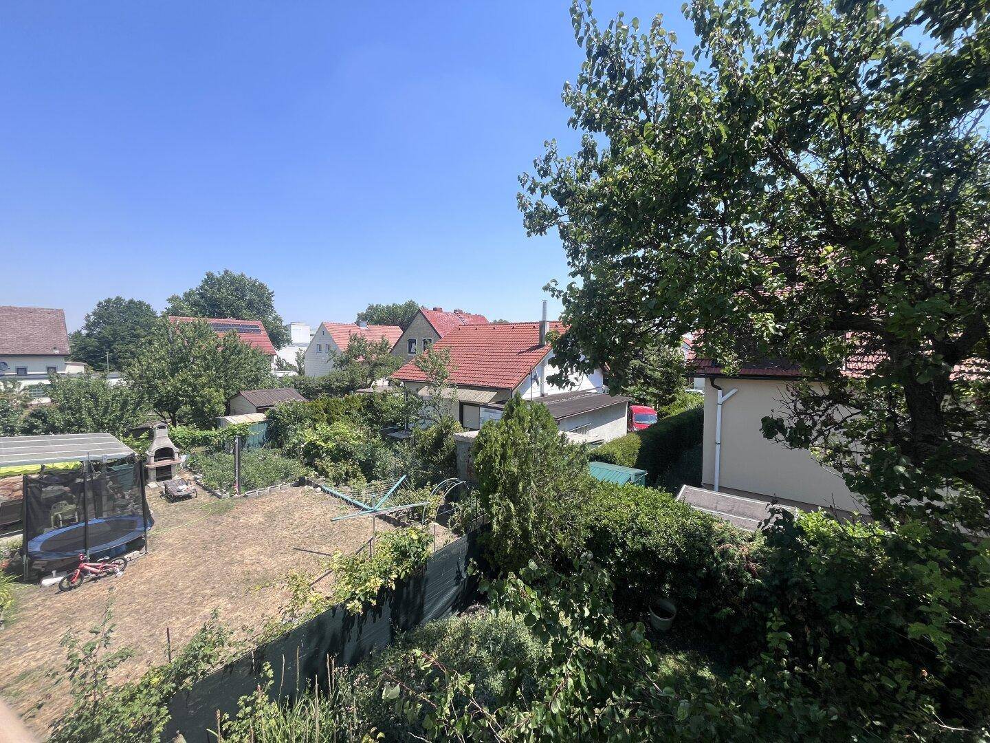 Blick von oben auf den Garten mit Trampolin und umliegende Häuser, sonniger Tag.