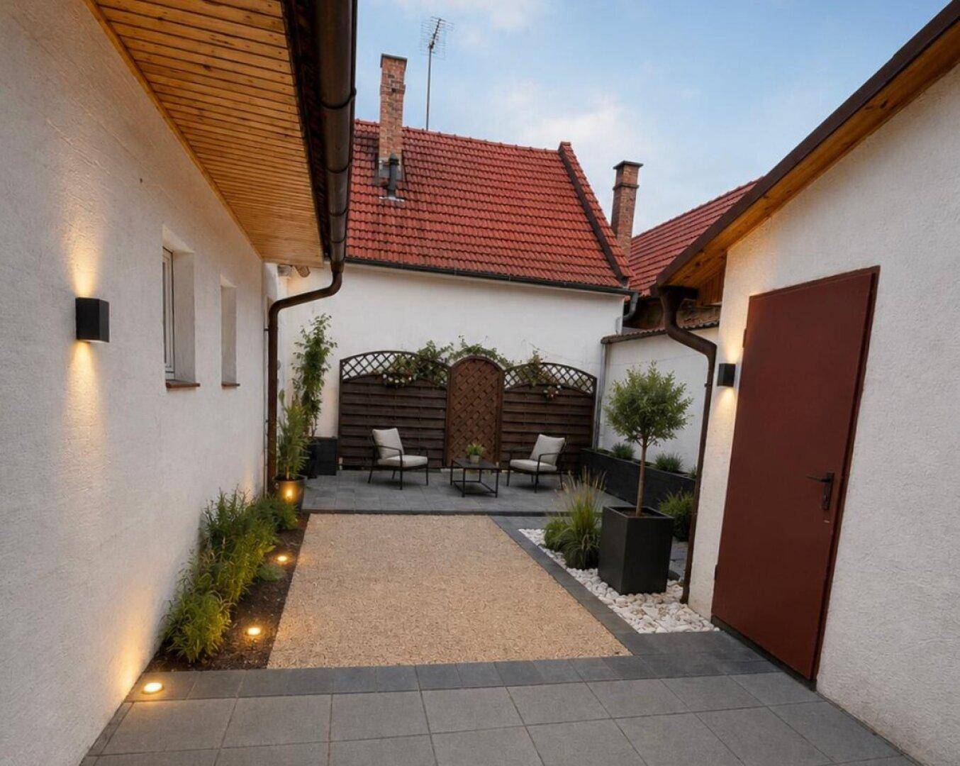 Gemütlicher Innenhof mit Sitzgelegenheiten, Kiesfläche und dekorativen Pflanzen in Töpfen.