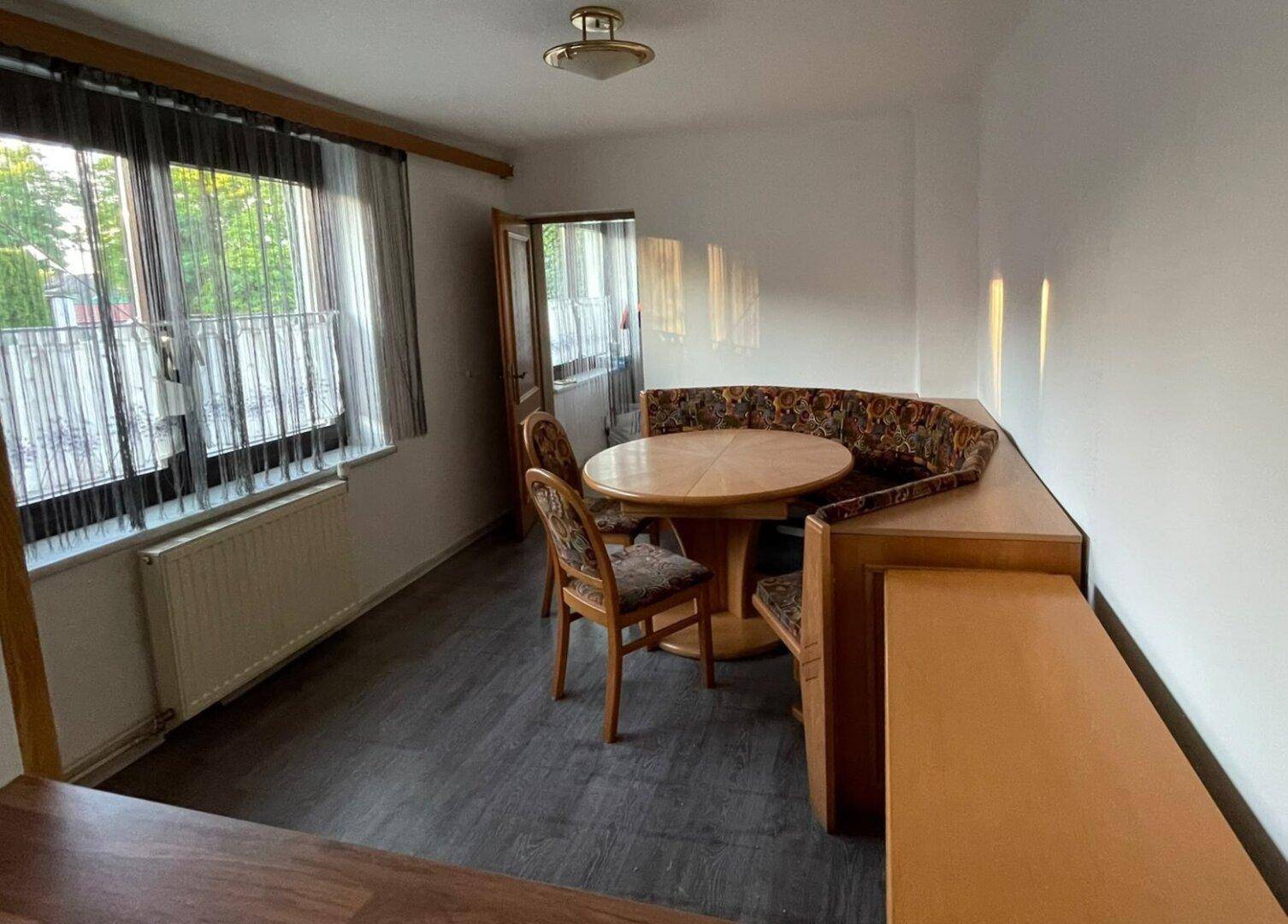 Essbereich mit Eckbank, Holztisch und Blick ins Grüne durch große Fenster.
