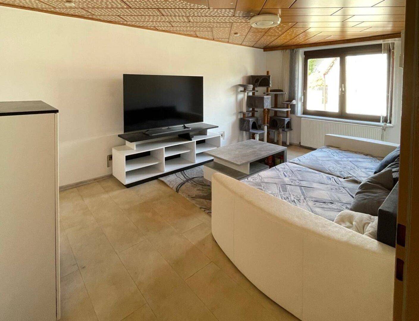 Wohnzimmer mit Holzbalkendecke, großem Fernseher und bequemer Couch.