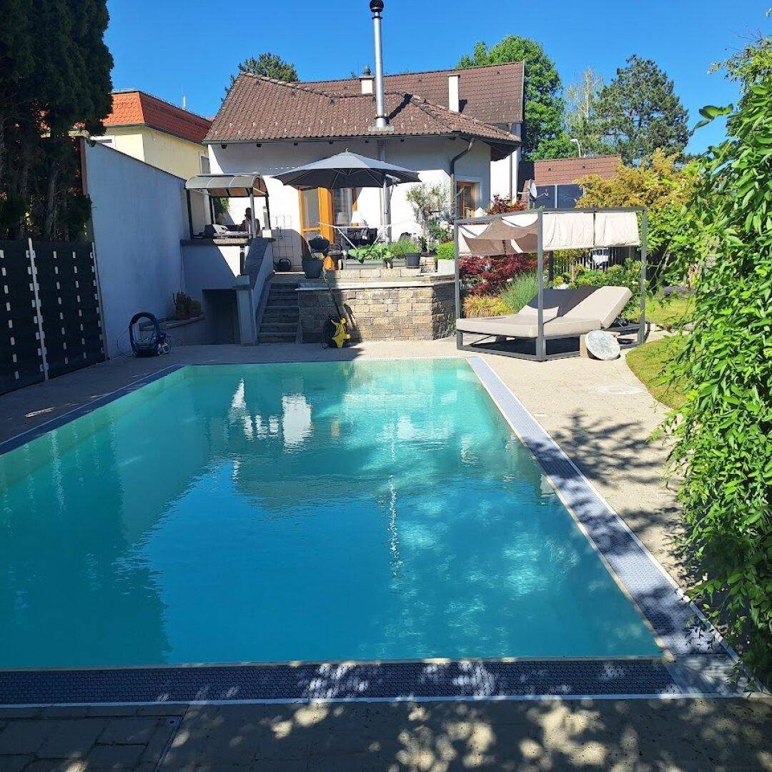 Großer Außenpool im Garten mit Liegefläche und Blick auf das Wohnhaus.