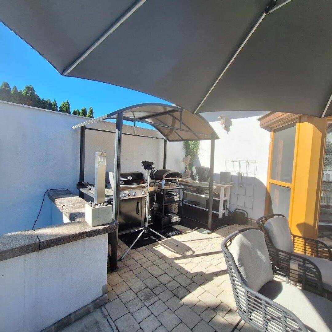 Gemütlicher Terrassenbereich mit Grillstation, Sonnenschirm und Sitzgelegenheiten im Freien.