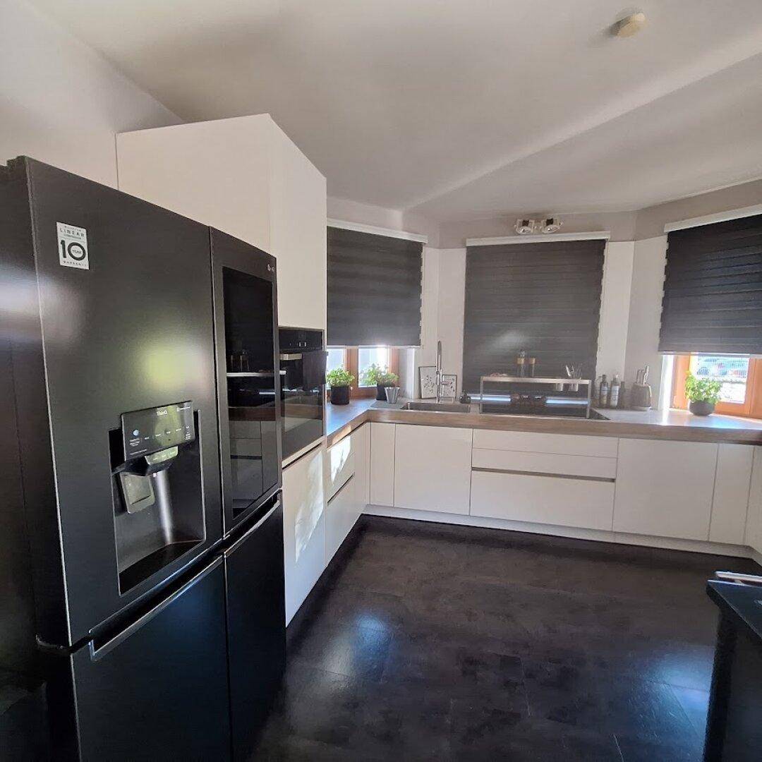 Moderne Küche mit schwarzem Side-by-Side-Kühlschrank, weißen Schränken und dunklem Holzboden.