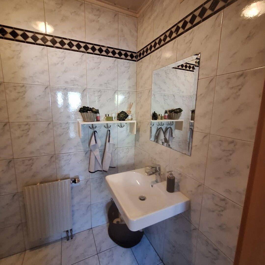 Kleines Gäste-WC mit hellen Fliesen, Wandwaschbecken und Heizkörper.