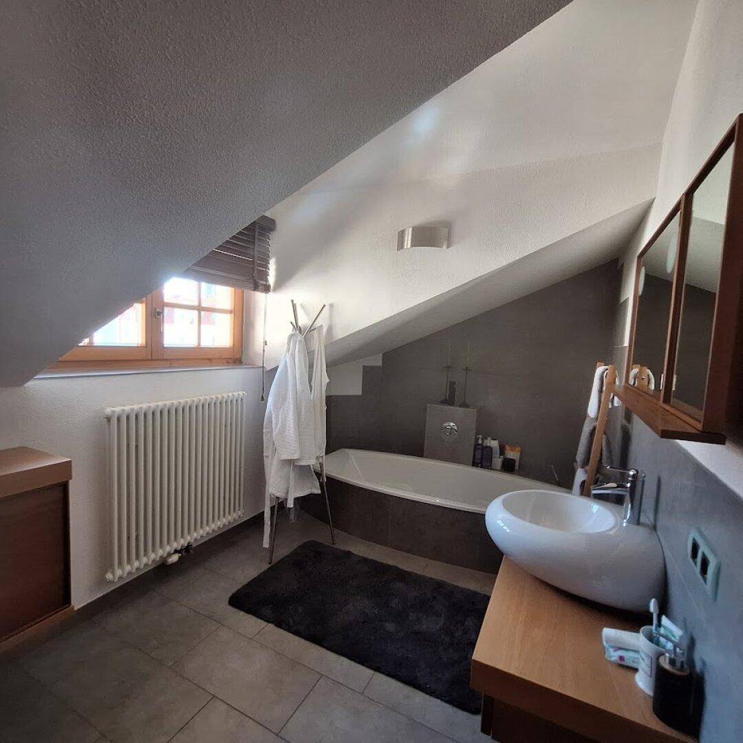 Modernes Badezimmer im Dachgeschoss mit Badewanne, Waschtisch und Dachfenster.