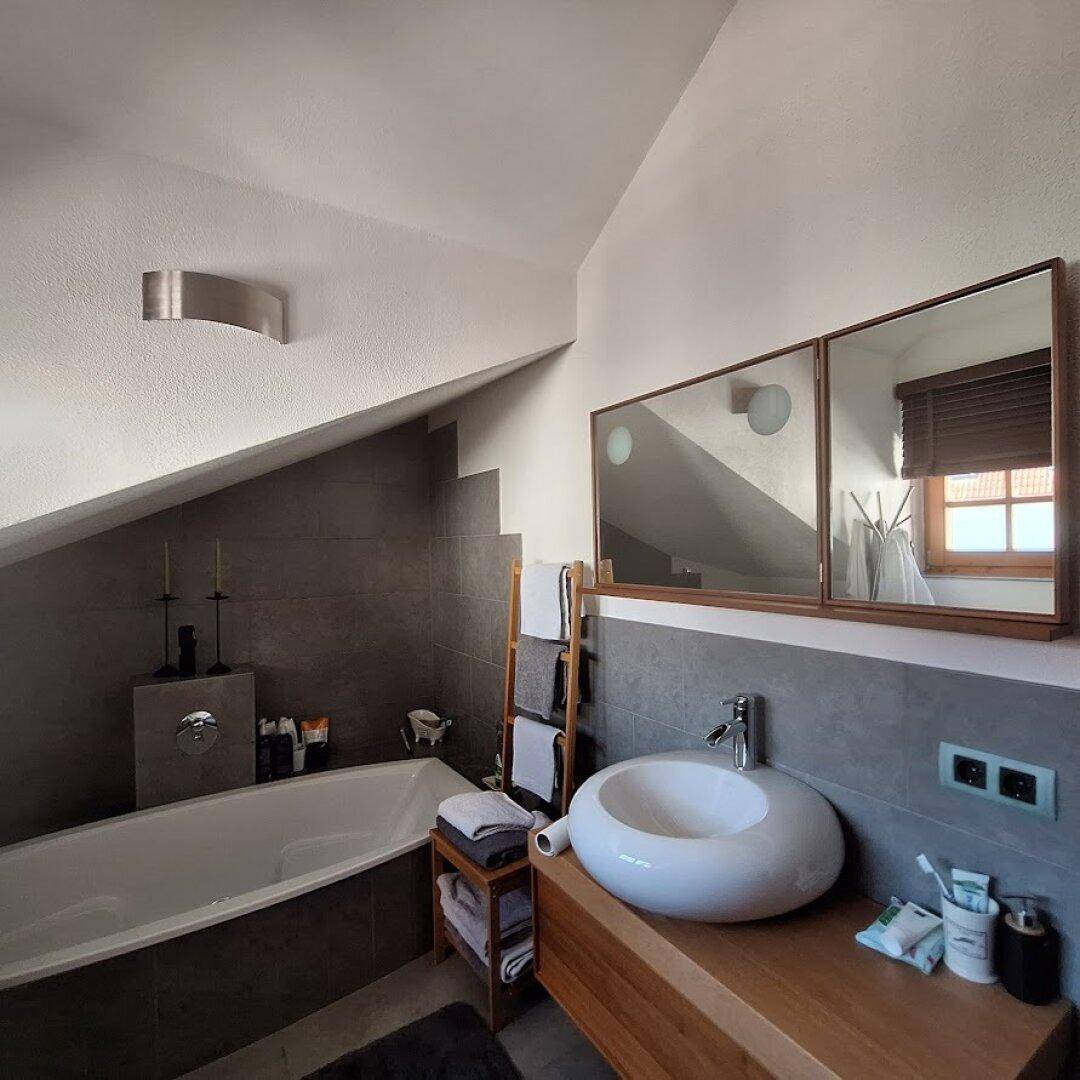 Stilvolles Badezimmer im Dachgeschoss mit Badewanne, Waschtisch und Spiegelschränken.