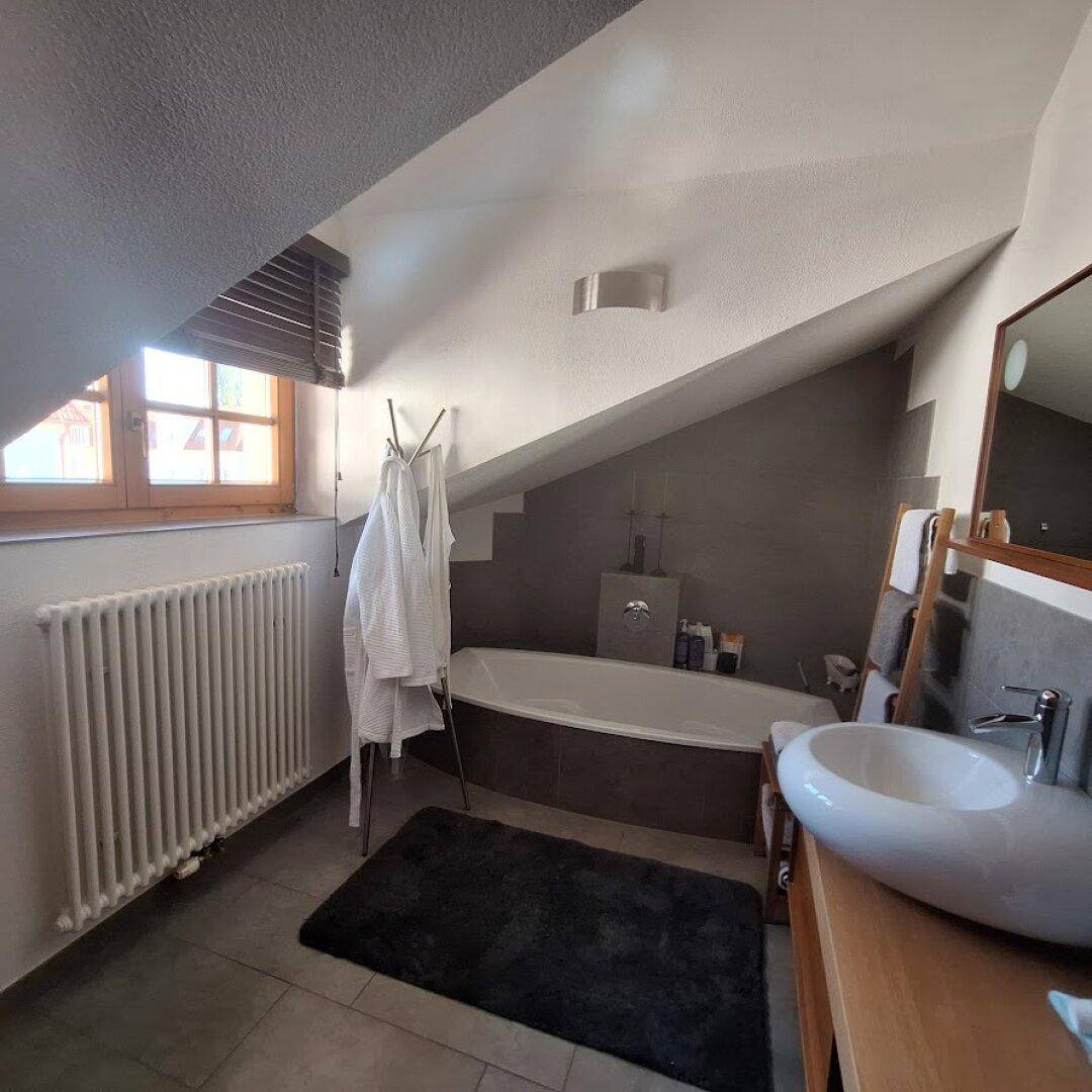 Helles Dachgeschoss-Badezimmer mit Badewanne, Heizkörper und Holzelementen.