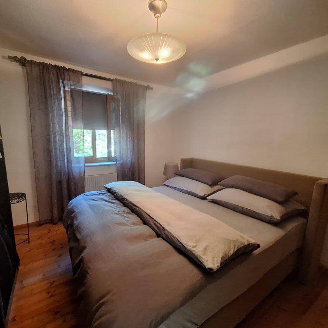 Schlafzimmer mit Doppelbett, Holzboden und Vorhängen am Fenster.