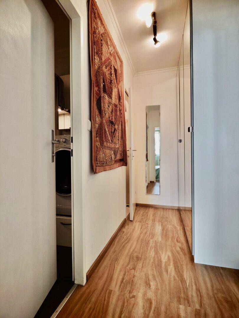 Heller Flur mit Holzboden, Wandteppich und Blick in den angrenzenden Waschraum.