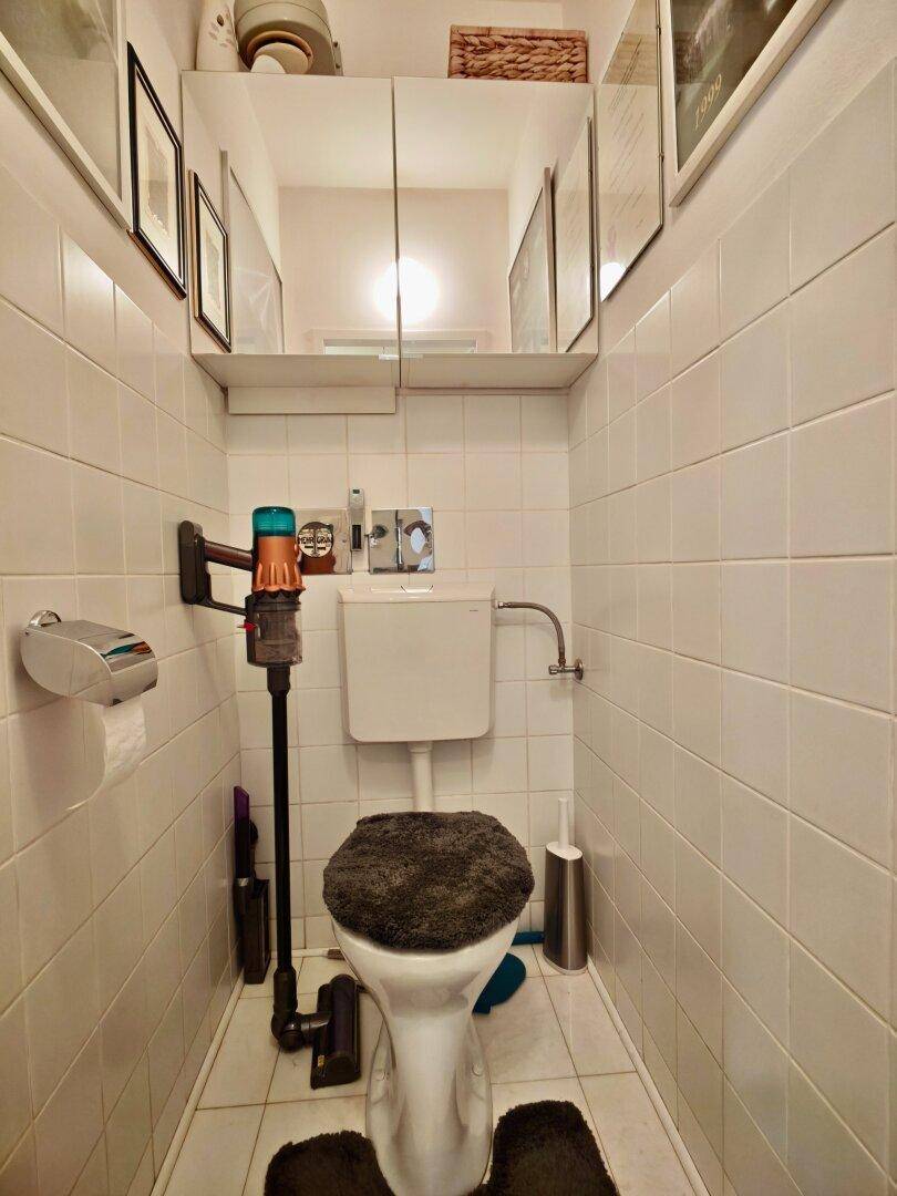 Kleines WC mit weißer Toilette, Fliesen und einem Spiegelschrank über dem Waschbecken.