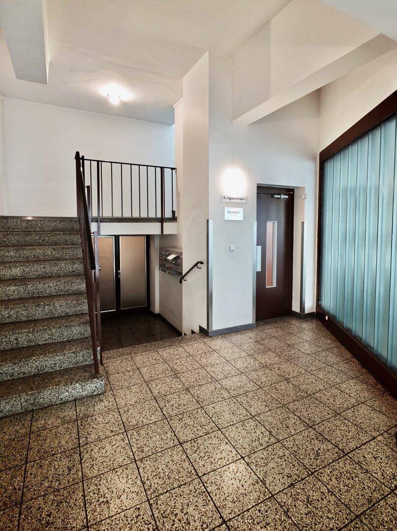Eingangsbereich eines Gebäudes mit Treppenhaus, Fliesenboden und Aufzug.
