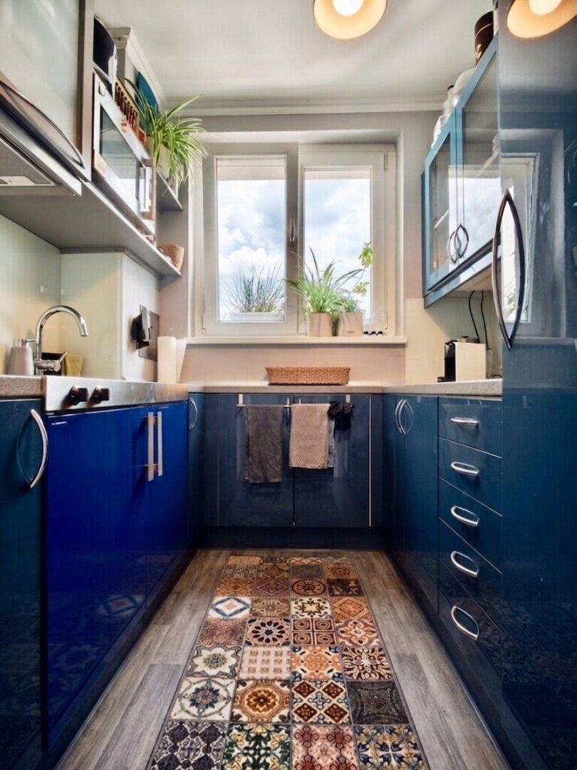 Moderne Küche mit blauen Hochglanzfronten, Fenster und farbenfrohem Teppichläufer.